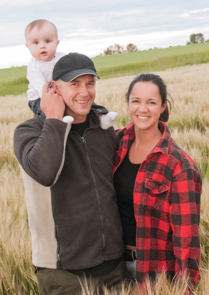 Middle age couple with a baby standing on a farm